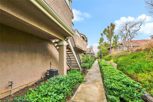 view of property exterior featuring stairway, stucco siding, a residential view, and central AC