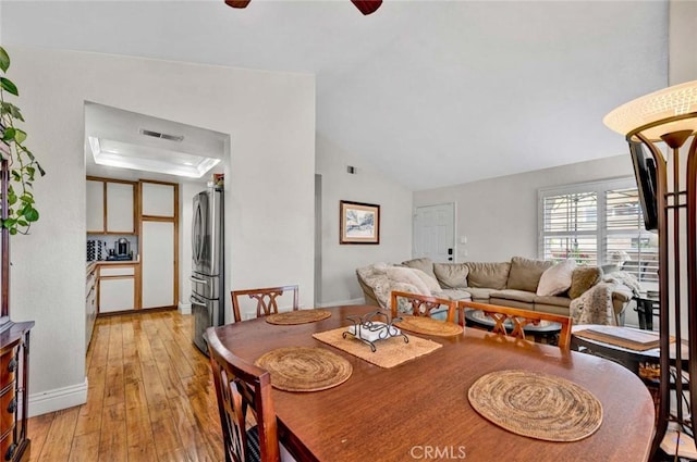 dining room with light wood finished floors, visible vents, baseboards, a tray ceiling, and a ceiling fan