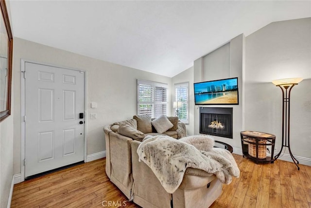 living area with light wood-style floors, lofted ceiling, a lit fireplace, and baseboards