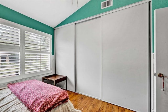 bedroom with vaulted ceiling, wood finished floors, visible vents, and a closet