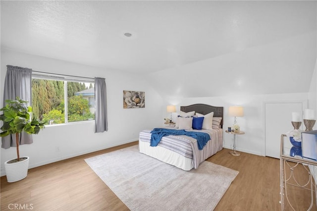 bedroom featuring lofted ceiling, baseboards, and wood finished floors