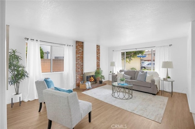 living room featuring light wood finished floors, a brick fireplace, and a textured ceiling