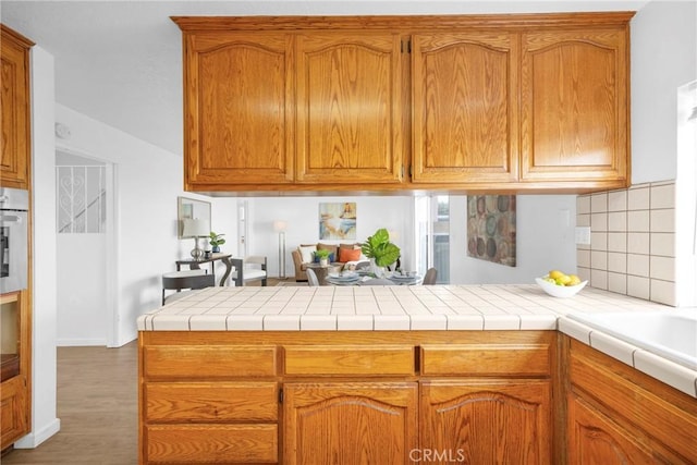 kitchen featuring a peninsula, light countertops, brown cabinets, and white oven