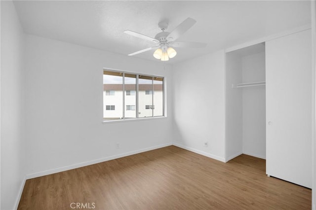 unfurnished bedroom with ceiling fan, wood finished floors, a closet, and baseboards