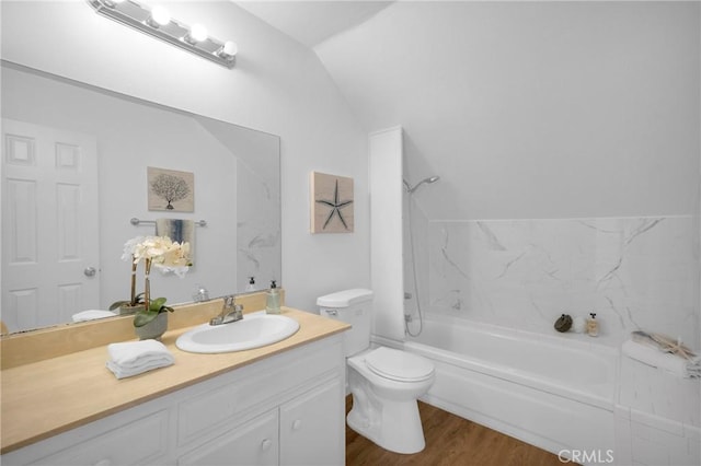 bathroom with toilet, wood finished floors,  shower combination, vanity, and vaulted ceiling