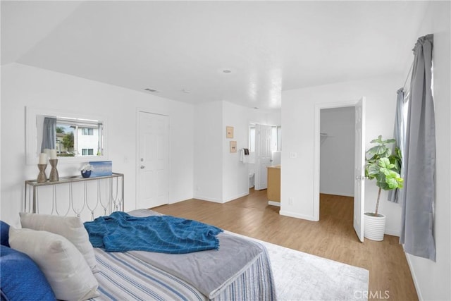 bedroom with wood finished floors, visible vents, baseboards, a spacious closet, and a closet