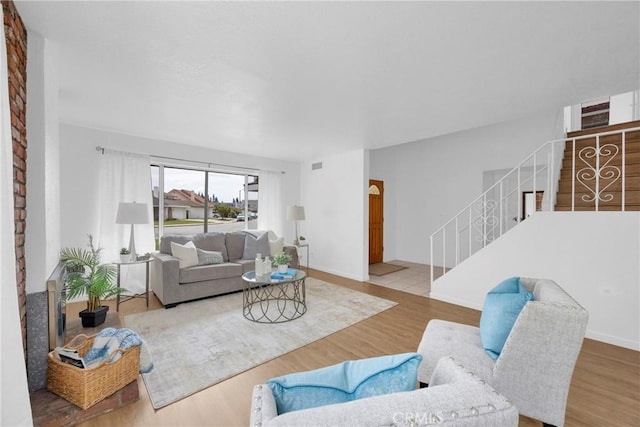 living room featuring stairway, baseboards, visible vents, and wood finished floors