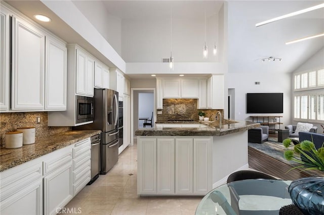 kitchen featuring open floor plan, white cabinets, stainless steel appliances, and dark stone counters