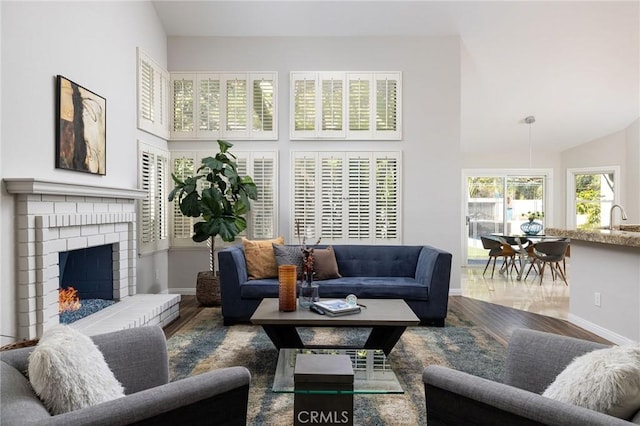 living room featuring a brick fireplace, wood finished floors, baseboards, and high vaulted ceiling