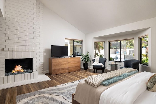 bedroom with a brick fireplace, wood finished floors, baseboards, and high vaulted ceiling