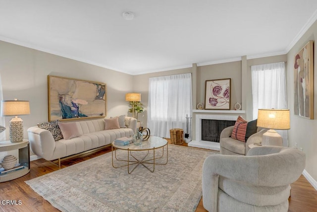 living area with ornamental molding, a fireplace, baseboards, and wood finished floors