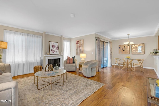 living room featuring baseboards, ornamental molding, wood finished floors, a fireplace, and a chandelier