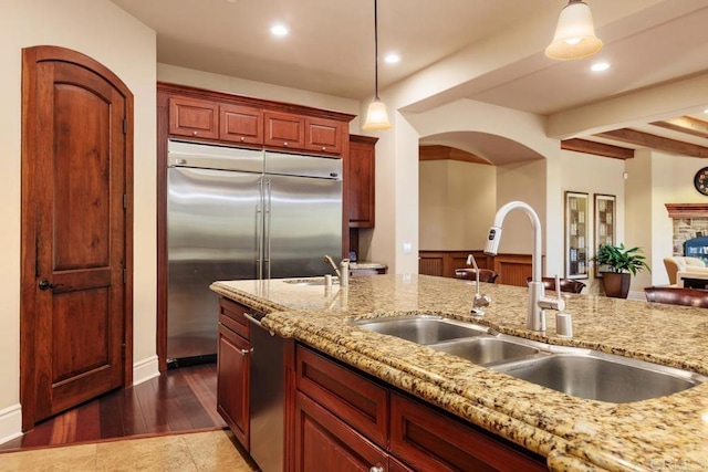 kitchen featuring hanging light fixtures, light stone counters, built in refrigerator, and a sink