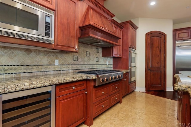 kitchen with built in appliances, light stone counters, beverage cooler, premium range hood, and tasteful backsplash