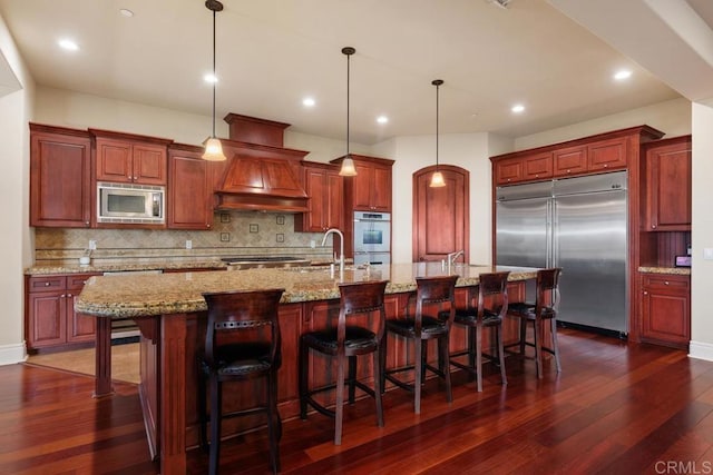 kitchen with decorative backsplash, dark wood-style floors, a large island, built in appliances, and custom exhaust hood