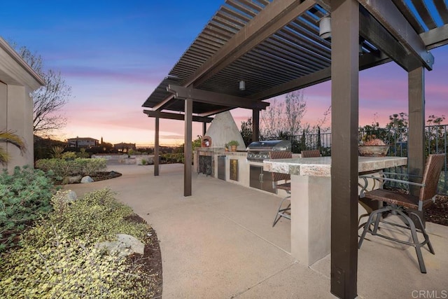 patio terrace at dusk with an outdoor kitchen, outdoor wet bar, fence, a grill, and a pergola