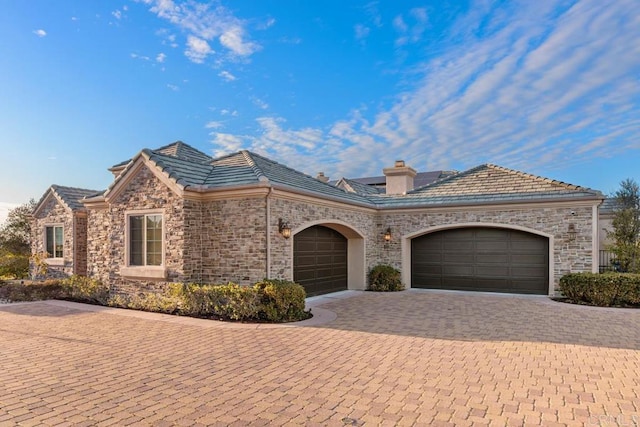 view of front facade featuring a garage, stone siding, a chimney, and decorative driveway