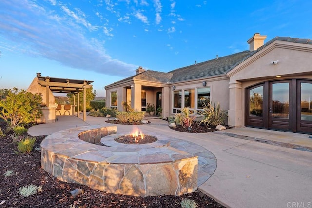 rear view of house with a patio area, an outdoor fire pit, a chimney, and stucco siding