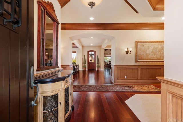 foyer featuring arched walkways, a decorative wall, dark wood-type flooring, and wainscoting