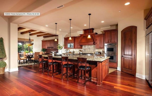 kitchen with tasteful backsplash, dark wood-style floors, custom range hood, appliances with stainless steel finishes, and light stone counters