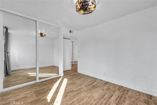 unfurnished bedroom with a closet, visible vents, baseboards, and wood finished floors