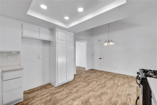 kitchen featuring a tray ceiling, stainless steel gas range, light wood-type flooring, and white cabinetry