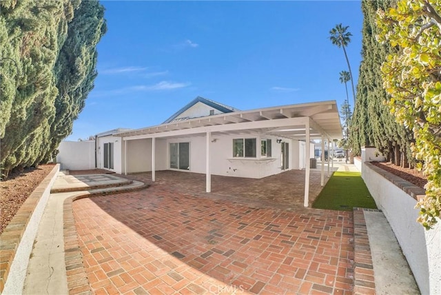 rear view of property featuring a patio area, fence, and stucco siding