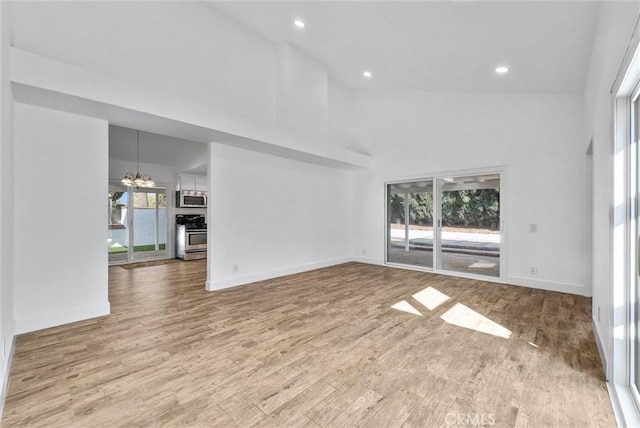 unfurnished living room featuring baseboards, wood finished floors, a towering ceiling, and a notable chandelier