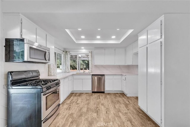 kitchen featuring light wood finished floors, white cabinets, a raised ceiling, stainless steel appliances, and light countertops