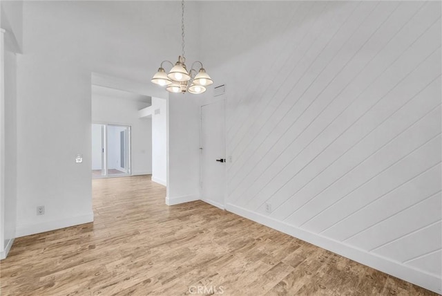 unfurnished dining area featuring baseboards, wood finished floors, and a notable chandelier