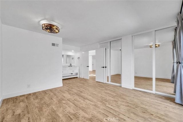 unfurnished bedroom featuring a sink, wood finished floors, visible vents, baseboards, and two closets