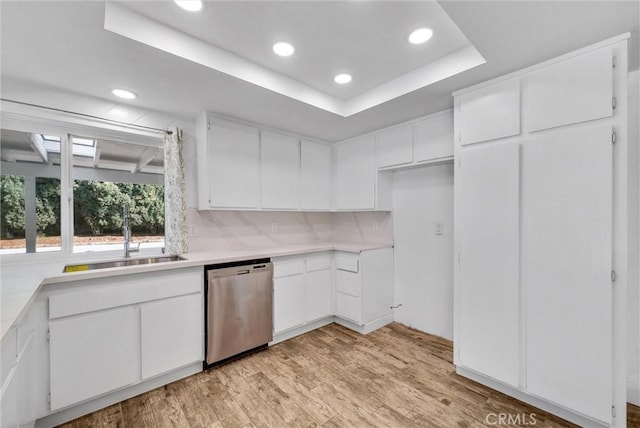 kitchen featuring a raised ceiling, dishwasher, light wood-style flooring, light countertops, and a sink