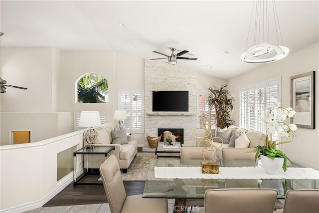 living room featuring a stone fireplace, vaulted ceiling, and ceiling fan