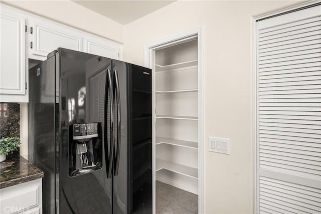 kitchen with tile patterned flooring, black fridge with ice dispenser, dark stone countertops, and white cabinetry