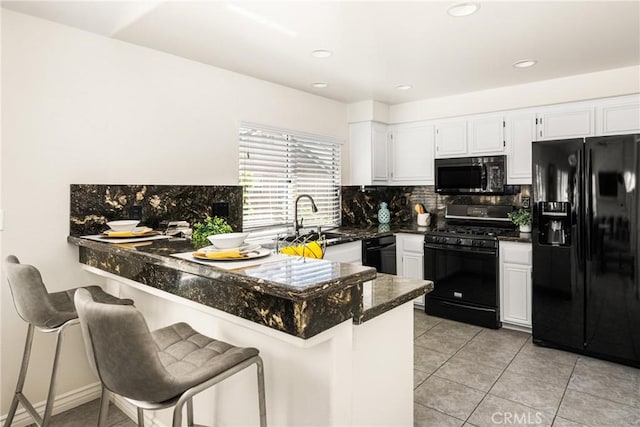 kitchen with decorative backsplash, a peninsula, white cabinets, black appliances, and a sink