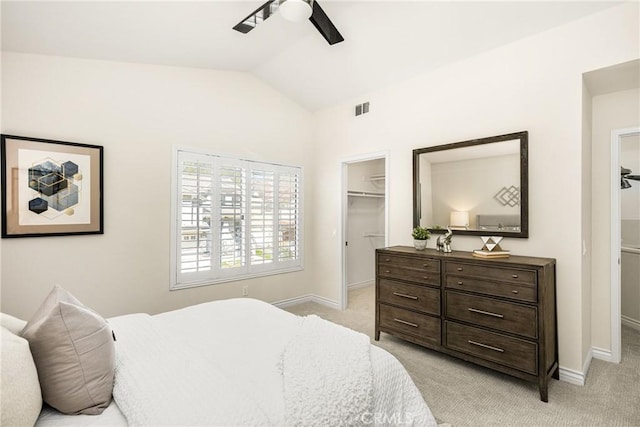 bedroom with a walk in closet, lofted ceiling, visible vents, and light carpet
