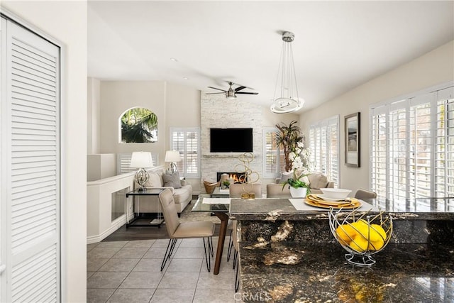 tiled dining room with a wealth of natural light, a stone fireplace, a ceiling fan, and lofted ceiling
