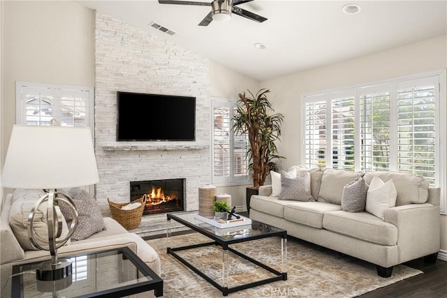 living area featuring visible vents, ceiling fan, vaulted ceiling, a stone fireplace, and wood finished floors
