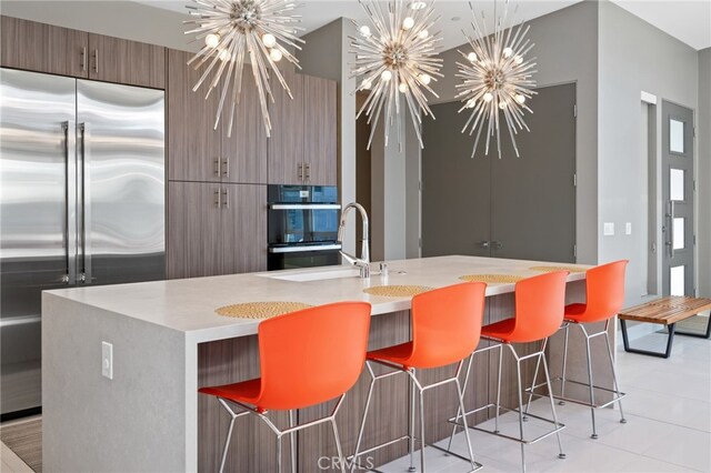 kitchen with a breakfast bar, light countertops, stainless steel built in fridge, and a notable chandelier