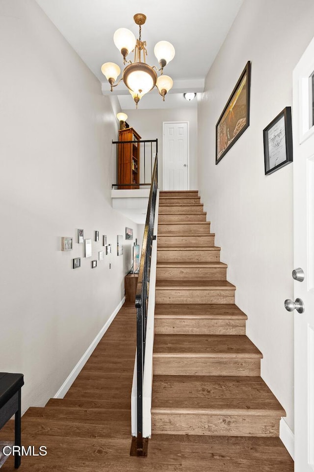 stairway featuring a notable chandelier, baseboards, and wood finished floors