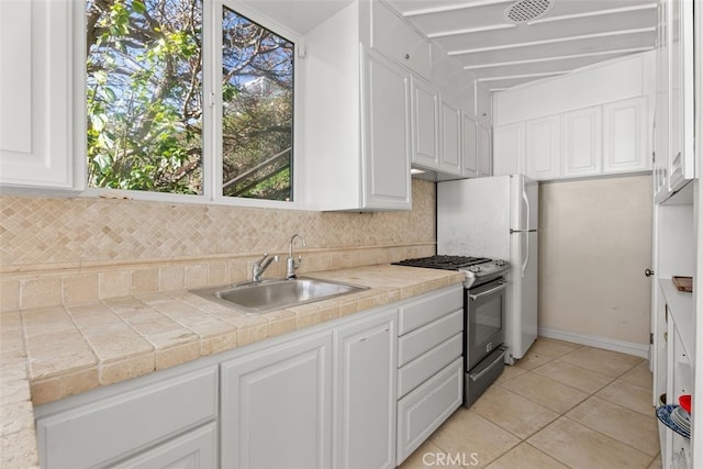 kitchen with light tile patterned floors, a sink, white cabinets, decorative backsplash, and stainless steel gas stove