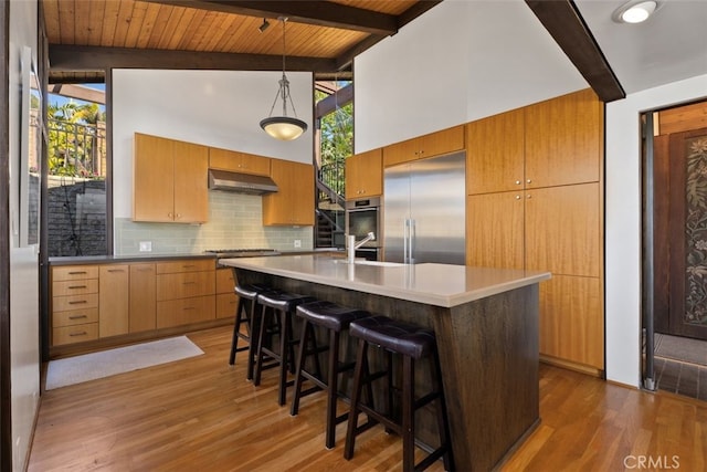 kitchen with decorative backsplash, appliances with stainless steel finishes, dark wood-type flooring, under cabinet range hood, and beam ceiling