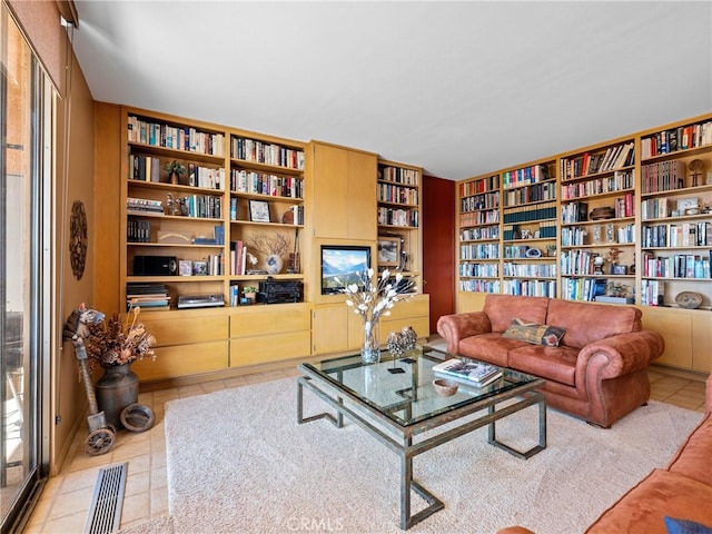 living area with wall of books, visible vents, and tile patterned floors