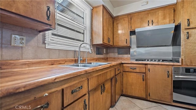 kitchen with light tile patterned floors, brown cabinetry, a sink, gas cooktop, and oven