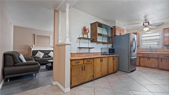 kitchen featuring light tile patterned floors, stainless steel appliances, light countertops, brown cabinetry, and ornate columns