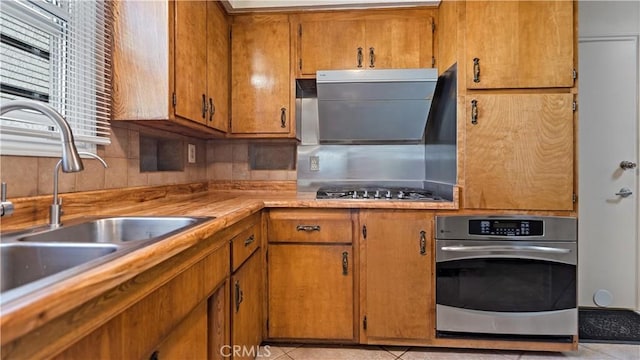 kitchen featuring light tile patterned floors, light countertops, appliances with stainless steel finishes, brown cabinetry, and a sink