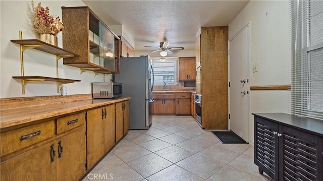 kitchen with open shelves, appliances with stainless steel finishes, a ceiling fan, brown cabinetry, and light tile patterned flooring