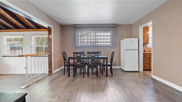 dining room featuring a textured ceiling, wood finished floors, and baseboards