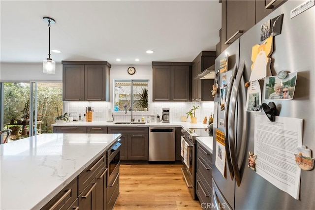 kitchen featuring appliances with stainless steel finishes, a sink, light wood finished floors, and decorative backsplash