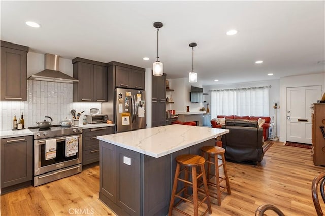 kitchen with stainless steel appliances, a kitchen island, light wood-style floors, decorative backsplash, and wall chimney exhaust hood